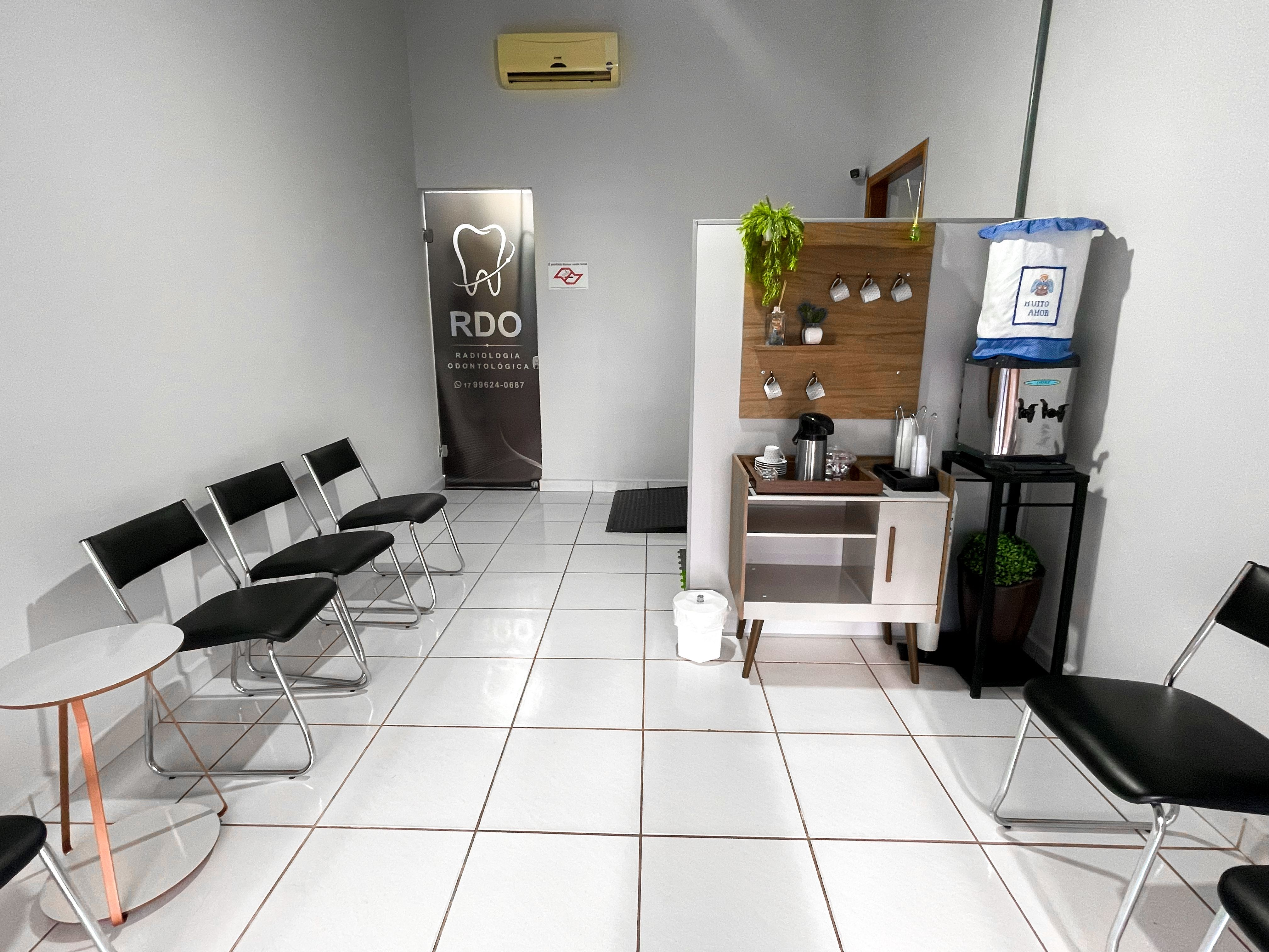 Sala de espera com cadeiras pretas, mesa lateral e cantinho do café.
